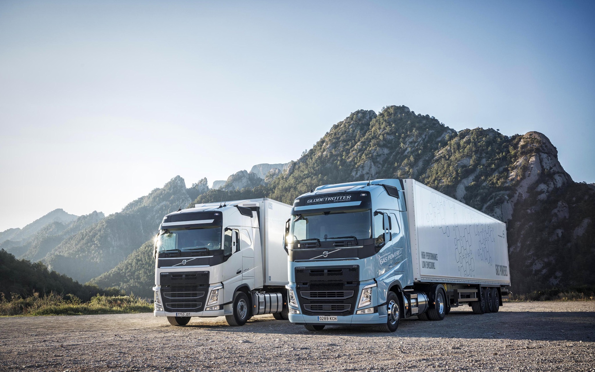 Two heavy goods trucks with cargo trailers in a mountain setting